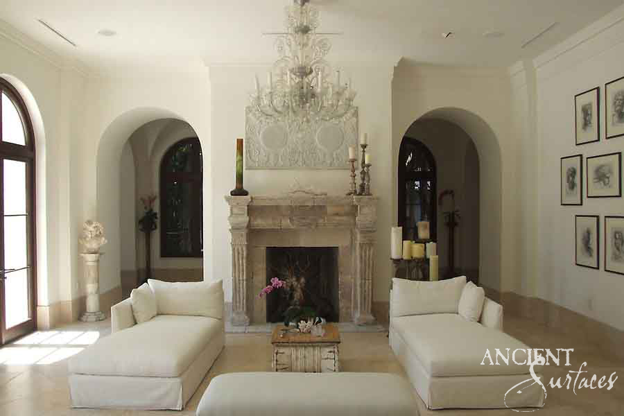 Weathered reclaimed limestone fireplace mantel centred between two plaster arches in a white salon