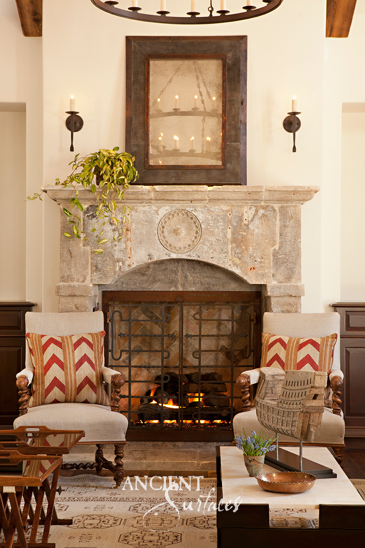 Antique reclaimed limestone fireplace mantel with a carved rosette medallion above a lit fire