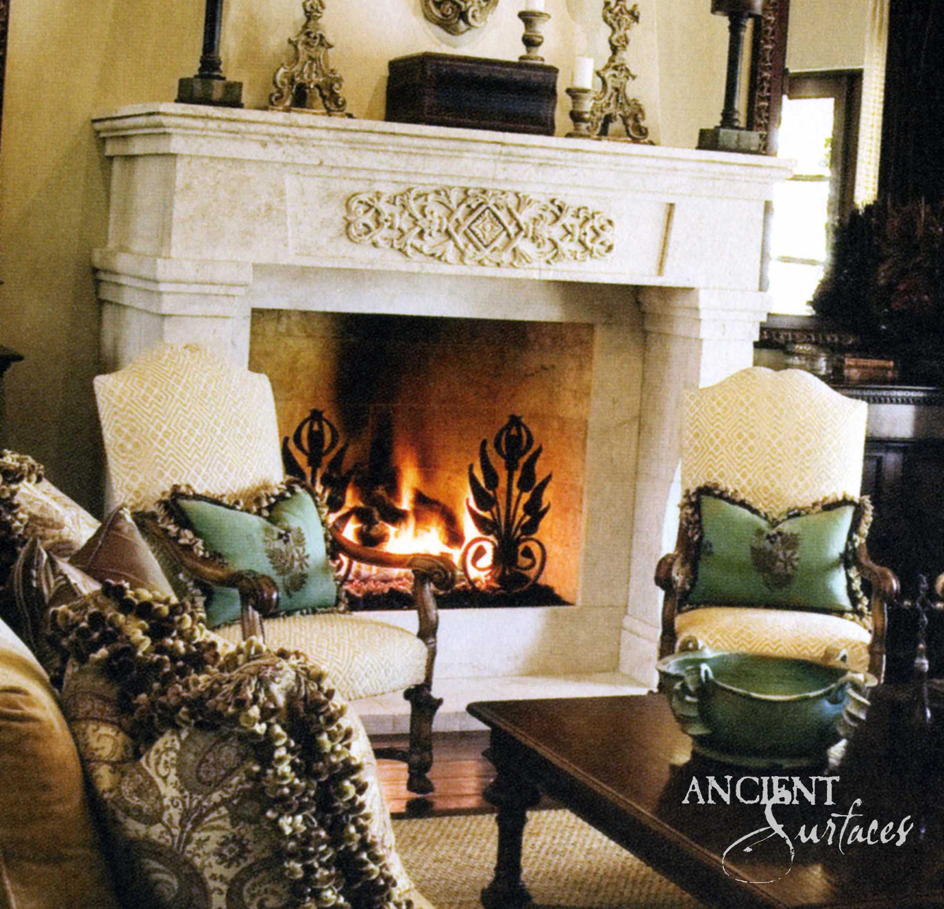 Ivory reclaimed limestone fireplace mantel with a carved cartouche medallion above a lit fire